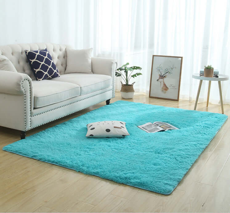 Bright turquoise silky fluffy carpet rug in cozy living room setting with sofa and decorative pillows.