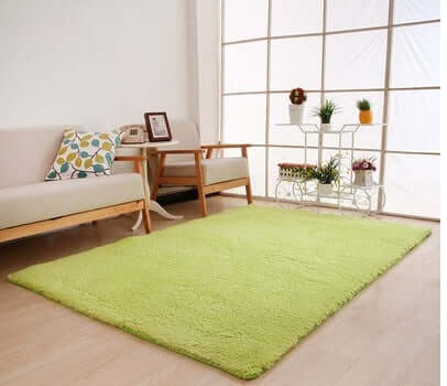 Living room with solid green rug on wooden floor, cozy seating, and decorative plant stand.