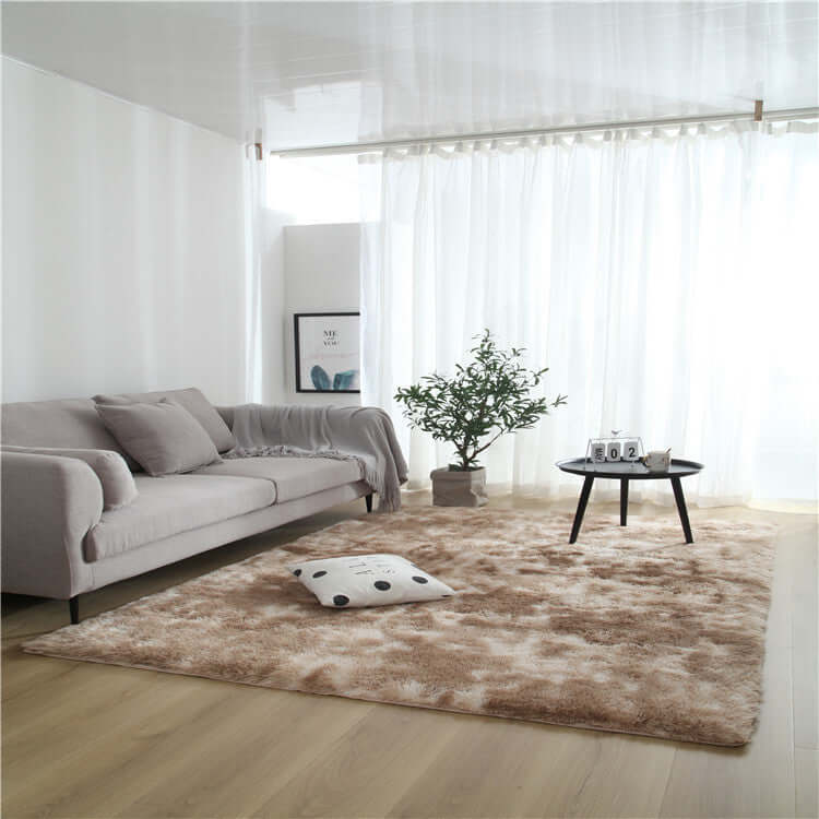 Cozy living room with a plush brown rug, gray sofa, plant, and coffee table, illuminated by natural light.