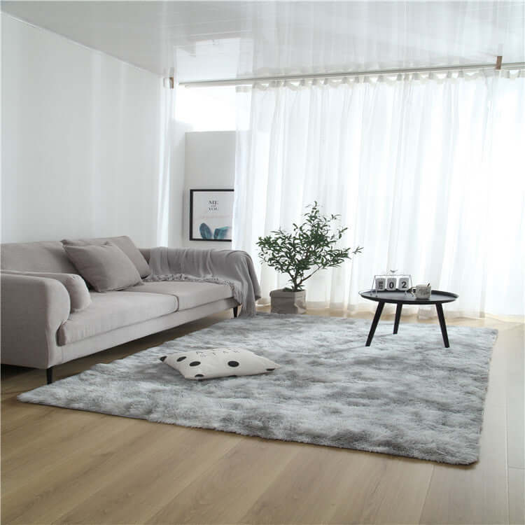 Cozy living room with a plush gray rug, light-colored sofa, coffee table, and indoor plant elegance.